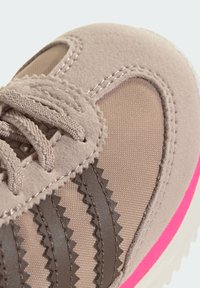 Béžová športová obuv zo semišu a sieťoviny. Výrazné tmavohnedé cikcak pruhy, ružové akcenty na podrážke a textúrované šnúrky.