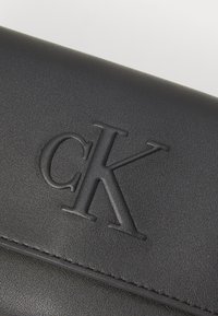 Portafoglio nero in pelle con logo "CK" in rilievo. Texture liscia, design minimalista, con cuciture orizzontali lungo il bordo.