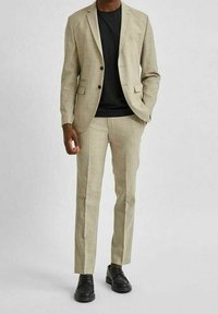 Beige rutigt kavaj med två knappar, parat med en svart t-shirt och matchande beige byxor; bärs med svarta skor.