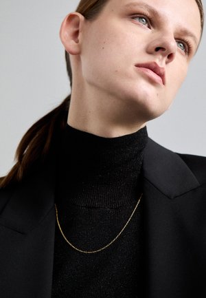 Schwarzer Strickrollkragenpullover kombiniert mit einem schwarzen Blazer, ergänzt durch eine zarte Goldkette; glatte Textur und elegantes Design.