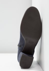 Bota de tobillo de ante azul marino con una suela de goma texturizada marrón, un pequeño tacón cuadrado y un cierre de cremallera lateral. Talla marcada como 37.