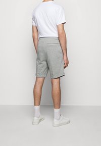 Shorts gris en tissu doux, avec une poche arrière. Portés avec un t-shirt blanc uni, associés à des baskets blanches et des chaussettes mi-mollet.