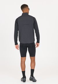 Svart lättviktscykeljacka med hög krage, långa ärmar och en bakficka. Bärs med svarta shorts och cykelskor.