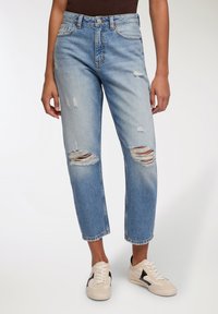 Jeans in denim blu chiaro con un fit rilassato, caratterizzati da diversi dettagli strappati e orli sfilacciati. Abbinate a sneaker beige.