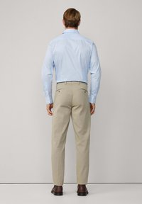 Light blue long-sleeve shirt with a collared neck paired with light beige trousers. Brown leather shoes visible. Standard fit, smooth texture.