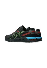 Des chaussures de sport noires avec des accents verts, une tige texturée, des détails rouges et gris, et une semelle bleue avec un élément réfléchissant au niveau du talon.