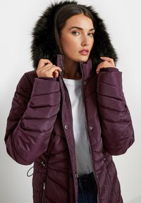 Lilla polstret jakke med faux fur hætte, diagonal quiltet tekstur, lynlås lukning og justerbar talje snøre detaljer.