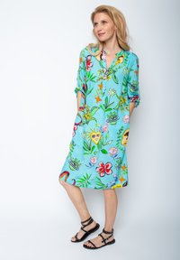 Ein hellblaues Kleid mit floralem und verspieltem Aufdruck, das kurze Ärmel, einen Kragen und eine lockere Passform aufweist. Mit schwarzen Riemchensandalen kombiniert.