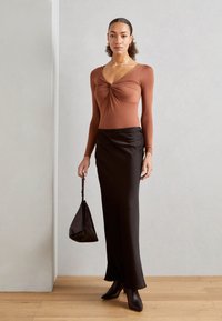 Ilga rankovė rust spalvos bodysuit su suktiniu priekyje, derinama su juoda satino maksi sijonu, elegantiškais kulkšnies batais ir maža juoda rankine.