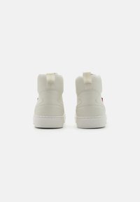 Vysoké tenisky z off-white syntetického materiálu s textúrovanou pätou, s malým červeným logom na stranách a plochou bielou podrážkou.