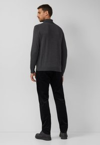 Ciemnoszary dziergany sweter z wysokim kołnierzem, w połączeniu z czarnymi sztruksowymi spodniami i czarnymi butami, widziany od tyłu na jednolitym tle.