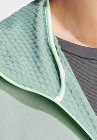 Chaqueta atlética verde claro con un cuello texturizado en patrón hexagonal y una capa interna suave, combinada con una camiseta gris.