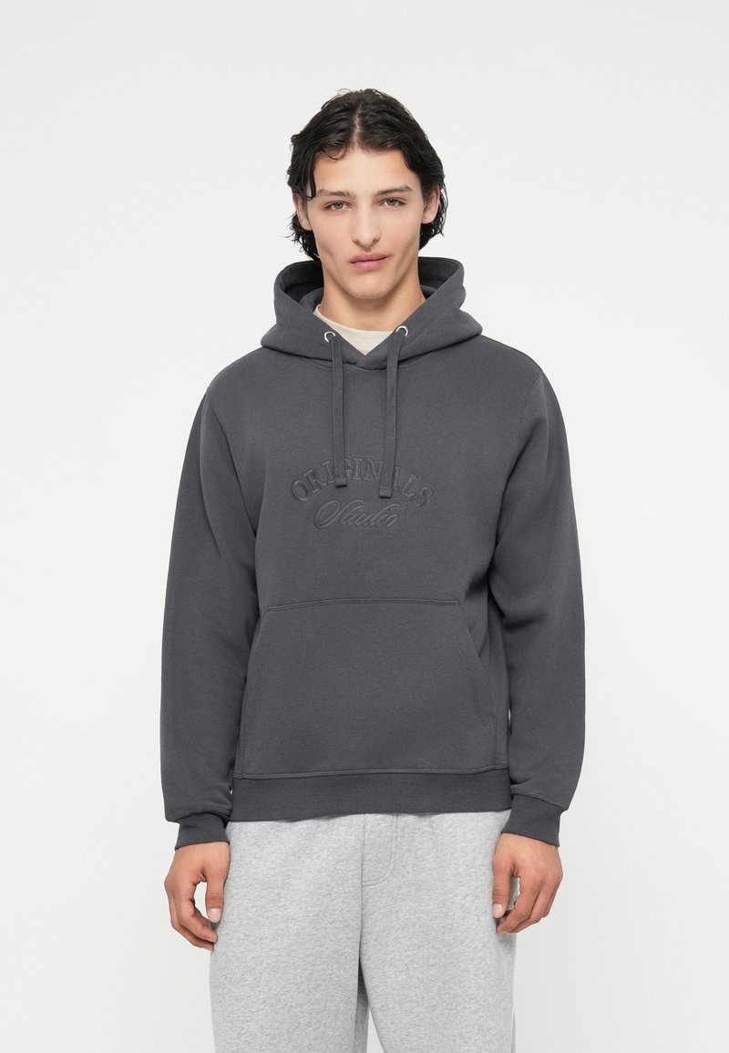 Sudadera gris con bolsillo canguro, capucha ajustable con cordón, y logo en relieve. Tejido suave con un corte relajado y puños de canalé.