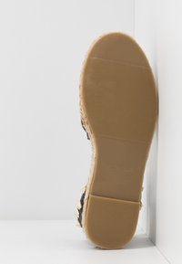 Suela de sandalia con relieve de goma, talla 4, estampado "Hecho en China", borde visible de yute y tachuelas metálicas en los lados superiores negros.