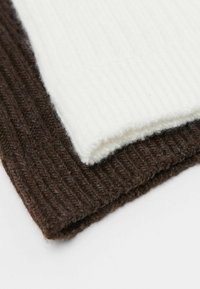 Dwa kawałki dzianiny, jeden brązowy, a drugi biały, z wyraźną strukturą prążkową i miękkim, puszystym wykończeniem. Każdy kawałek ma czysty, prosty brzeg.