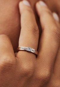 Bague en or rose avec une pierre ronde centrale et de petites pierres d'accent le long de l'anneau, textures lisses avec une surface polie.