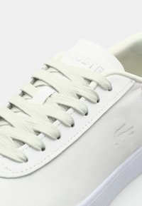 Baskets en cuir blanc avec lacets blancs, logo embossé discret sur le côté et coutures visibles le long du bord.