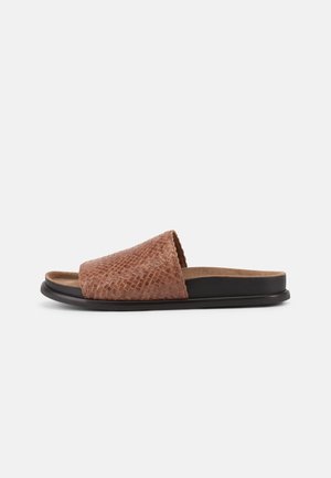 Brun tekstureret slidesandal med bred rem og sort sål på en ensfarvet lysegrå baggrund.