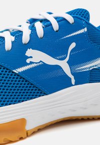 Blue sneaker featuring a mesh upper, white accents, a prominent logo, and a textured rubber sole with orange detailing.
