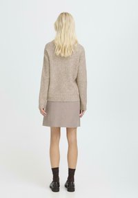 Beżowy sweter dzianinowy z długimi rękawami, zestawiony z prążkowaną jasnobrązową spódnicą. Dodatki to ciemnobrązowe skarpetki i czarne buty.