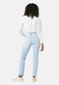 Hellblaue Denim-Jeans, gerade geschnitten, mittlere Leibhöhe, Gesäßtaschen mit dezentem Stickmuster. Kombiniert mit einem weißen Hemd mit Knöpfen und hellen Sneakers.