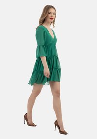 Rochie verde din chiffon cu decolteu în V, design în straturi și mâneci tip clopot. Asortată cu pantofi cu toc înalte cu imprimeu animalier în nuanțe de bej și marron.