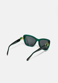 Ochelari de soare supradimensionați, verzi, cu brațe negre înguste, accentuați cu elemente de aur și lentile de culoare gri închis. Materialul este plastic lucios.