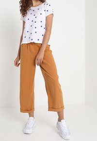 Top corto de manga corta blanco con lunares azules, combinado con pantalones holgados de color mostaza con puños enrollados y zapatillas blancas. Conjunto simple y casual.