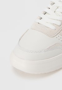 Hvide lædersneakers med beige ruskindsdetaljer, tekstureret overflade, rund tå og flade snørebånd, der har perforeringer og en glat gummisål.