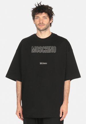 T-shirt nera oversize in cotone. Presenta la scritta "Moschino" in strass e "Milano" sotto. Maniche corte e design a collo rotondo.