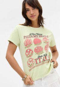 Light green cotton t-shirt featuring a graphic print of pizza designs and text in red and black. Round neckline, short sleeves.