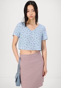 Top cortado azul claro con mangas cortas y escote en V, con un patrón floral en violeta y blanco, combinado con una falda texturizada rosa.