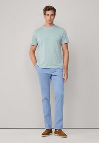 Light blue cotton chinos paired with a short-sleeve, light green striped T-shirt. Brown slip-on shoes complete the casual outfit.