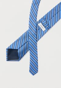 Corbata de seda azul con rayas diagonales en azul claro y oscuro, con un forro interior azul marino. Etiquetas visibles con el nombre de la marca "LES DEUX".
