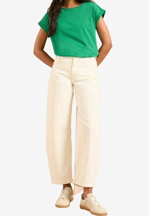 Grøn t-shirt med korte ærmer, beige bukser med vide ben og beige sneakers. Outfit'et har en afslappet pasform og glatte teksturer.