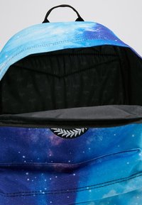 Reppu, jossa on sinivioletti galaksikuvio, kangasrakenteen, nyörisuljin ja musta sisustus, jossa on toistuva logokuva.
