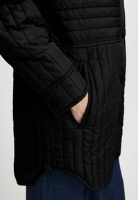 Chaqueta de plumas negra acolchada con un alto collar, puños abotonados y bolsillos laterales; fabricada en un tejido suave y ligero con un acabado texturizado.