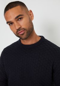 Navyblauer, gestrickter Pullover mit einem strukturierten Rautenmuster, ausgestattet mit einem Rundhalsausschnitt und gerippten Bündchen.