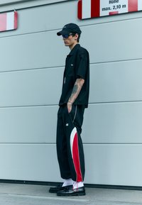 Black short-sleeve shirt, black track pants with white and red stripes, black shoes, white socks, black cap, and sunglasses.