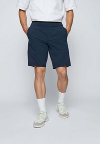 Námořnické modré šortky s elastickým pasem, bočními kapsami a hladkou, lehkou texturou, doplněné bílými ponožkami a teniskami.