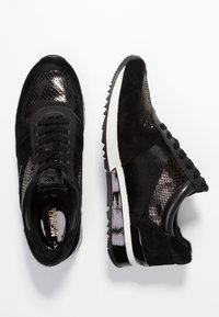 Black Michael Kors sneakers with mixed textures including patent leather, suede, and faux snakeskin, featuring white and black soles.