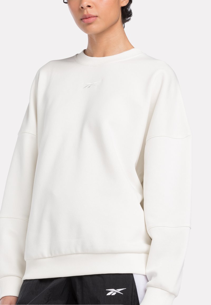 Weißer Pullover mit Rundhalsausschnitt und übergroßen Ärmeln, der ein dezentes gesticktes Logo auf der Brust und einen gerippten Saum aufweist.