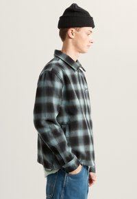 Czarna i turkusowa kurtka w kratę z kołnierzem, bocznymi kieszeniami i haftowanym logo. Slim fit w konstrukcji z teksturowanej bawełny.