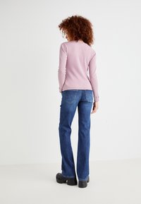Maglia a maniche lunghe a coste di un rosa chiaro, abbinata a jeans a zampa d'elefante blu. I jeans presentano tasche posteriori e sono completati da scarpe con tacco a piattaforma nere.