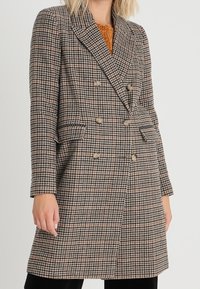Cappotto doppiopetto in un motivo a scacchi marrone e beige, realizzato in tessuto testurizzato, con rever a punta e due tasche frontali.