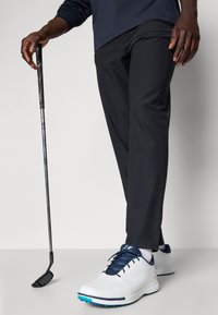 White golf shoes with blue accents, black golf pants, and a golf club, focusing on the shoe's laces and grip texture of the club.