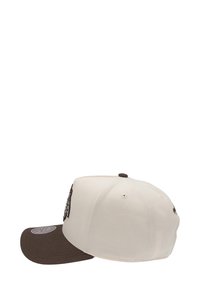 Casquette blanche avec une visière marron, ornée d'accents brodés à l'avant. Le matériau semble structuré, avec des trous de ventilation sur les côtés.