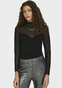 Schwarzer Langarm-Body mit transparentem Material im oberen Bereich, kombiniert mit funkelnden silbernen High-Waist-Hosen für einen texturierten Kontrast.