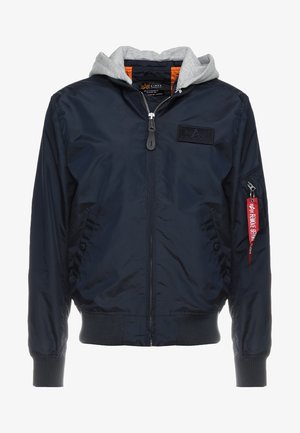 Námornícka bombová bunda so šedou kapucňou, zipsovým zapínaním, rebrovanými manžetami a nášivkou na hrudi. Obsahuje zipsovú kapsu s červeným štítkom.