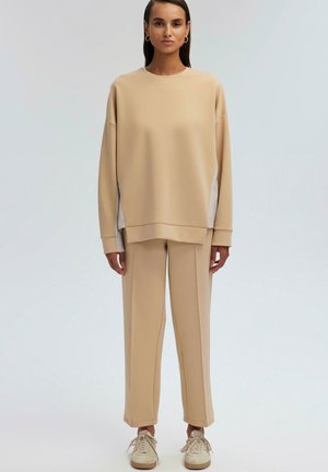 Sweatshirt beige à coupe décontractée et manches surdimensionnées, assorti à un pantalon fuselé. Les deux sont fabriqués dans un tissu doux et texturé.